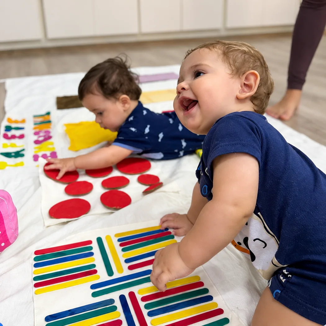 Duas crianças pequenas brincam com peças coloridas sobre um tecido branco