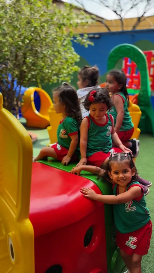 Crianças de uniforme verde sorrindo no escorregador do parquinho