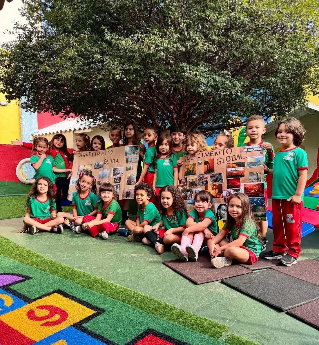 Turma do 2º período sentada no pátio, sob a árvore, com os cartazes de um projeto sobre o planeta